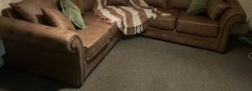 A brown corner sofa with a throw and green cushions